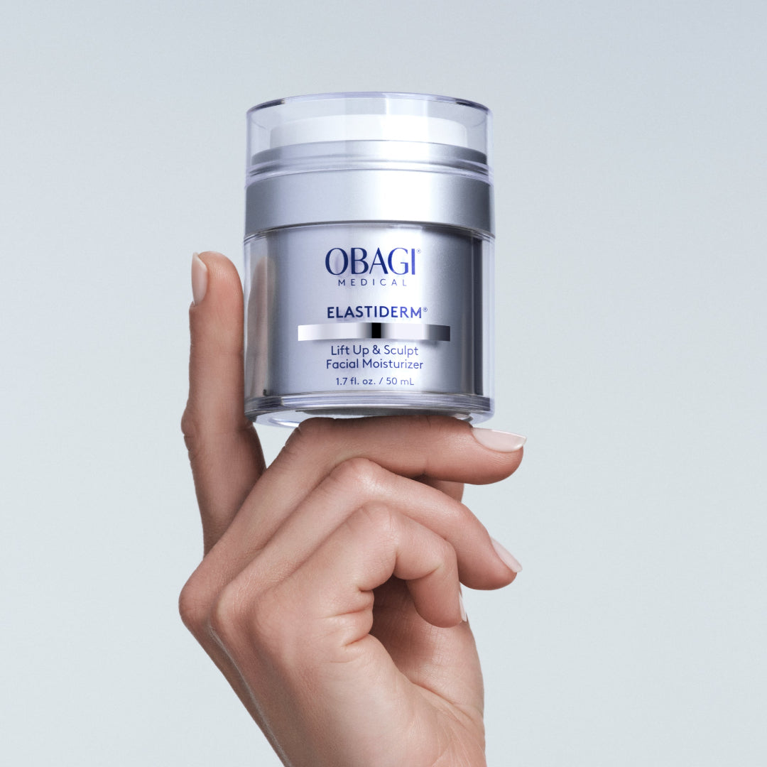 Hand holding a jar of Obagi Elastiderm cream against a light gray background