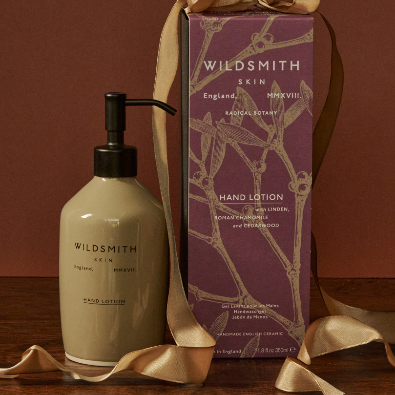Hand lotion bottle and packaging with gold ribbon on a wooden surface