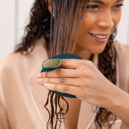 Woman with wet hair using a green hairbrush indoors