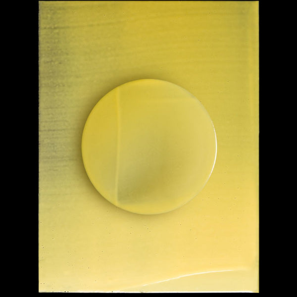 A translucent yellow circular gel or liquid drop centered on a square yellow sample card, photographed against a black background.