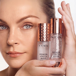 A close-up of a woman holding two Lyma skincare bottles, Power Youth Mist and Power Youth Mask, against a clean white background.
