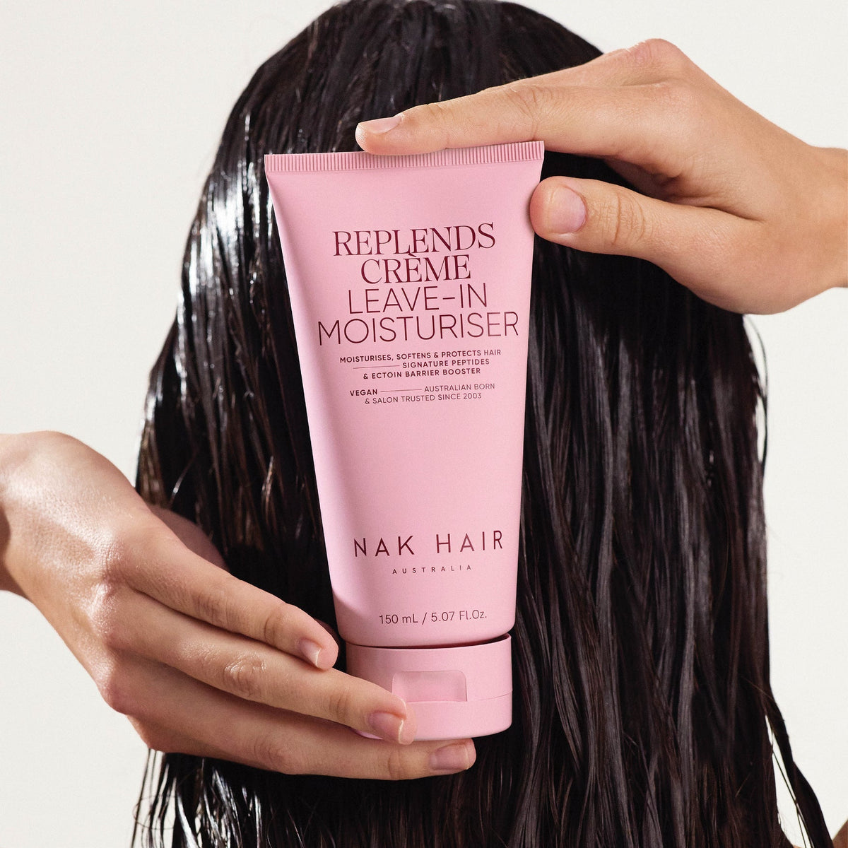 Person holding a pink tube of NAK HAIR Replends Creme Leave-In Moisturiser against a neutral background