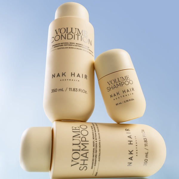 Nak Hair Volume Shampoo and Conditioner bottles stacked on a light blue background