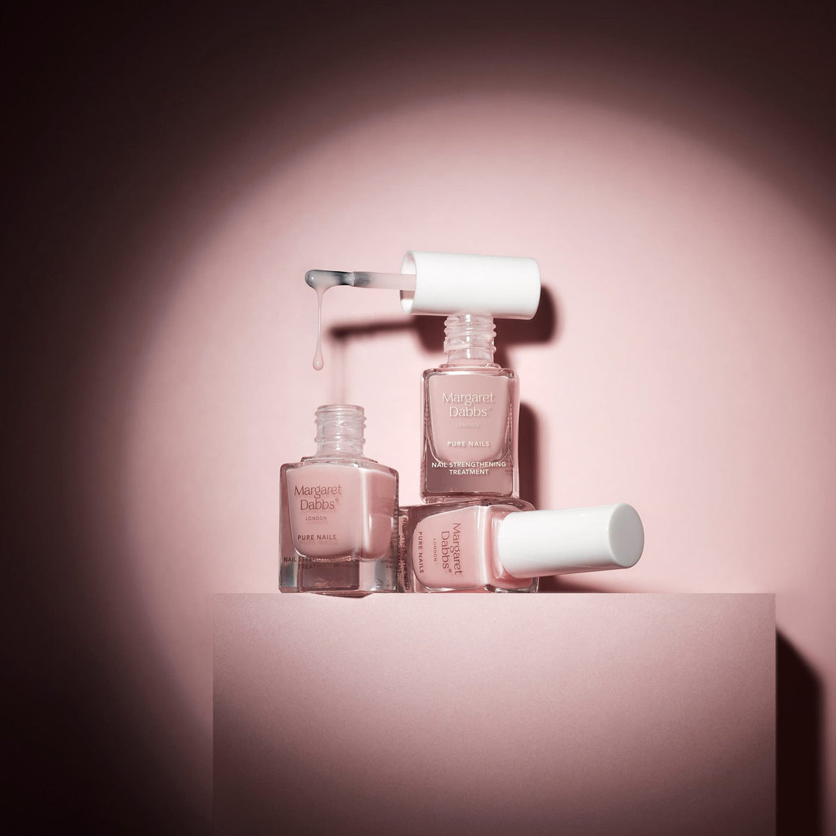 Set of nail polish bottles with a pink gradient on a matching pink background
