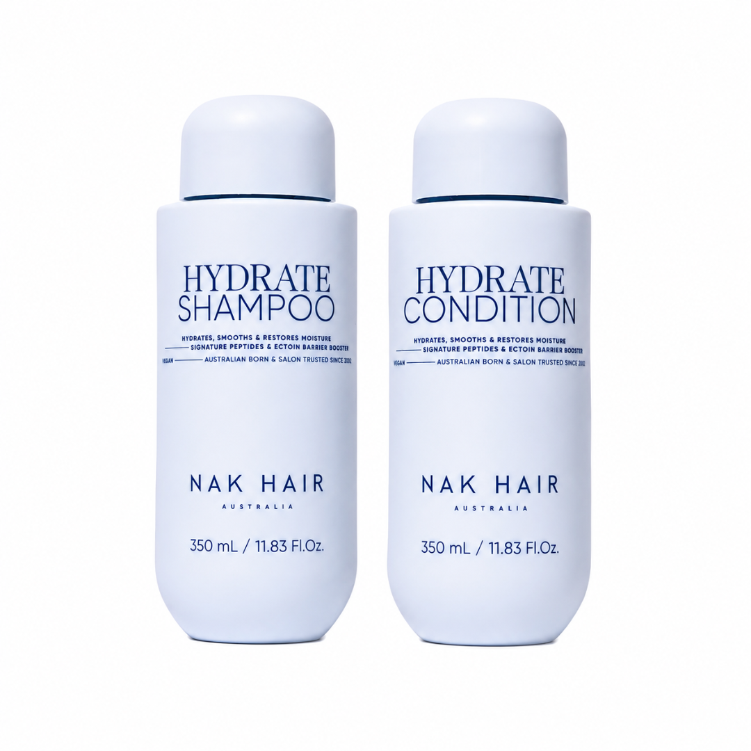 Two white cylindrical bottles of NAK Hair hair care products on a plain white background. The left bottle is labeled 'HYDRATE SHAMPOO' and the right bottle is labeled 'HYDRATE CONDITION'.