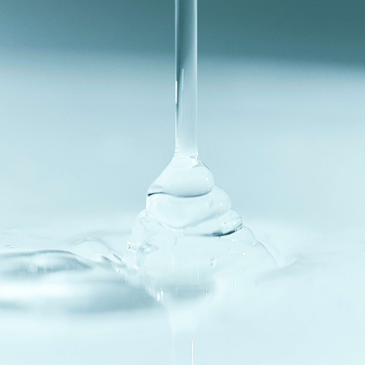 Close-up of a drop of clear liquid falling onto a reflective surface with a gradient blue background.