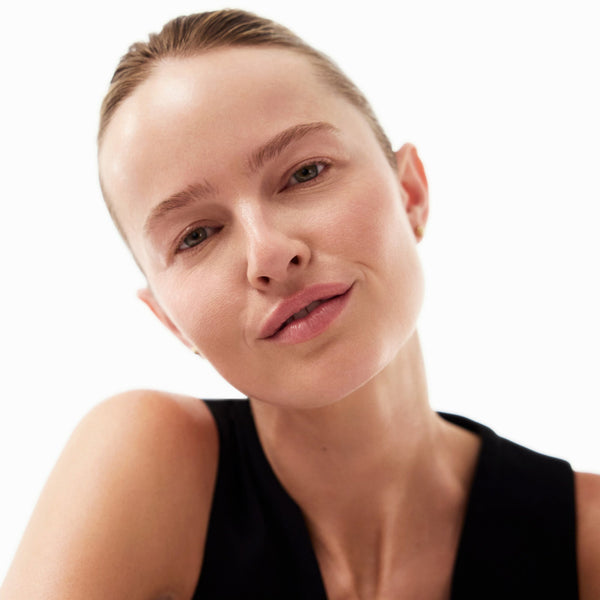 A close-up portrait of a woman with her hair pulled back, wearing a black sleeveless top against a plain white background.