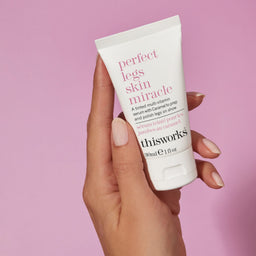 Hand holding a tube of 'perfect legs skin miracle' against a pink background