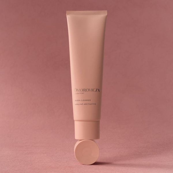 A single tube of Dhorovica Clear Skin Cleanser in a soft dusty pink color, standing upright on its cap against a matching solid pink background.