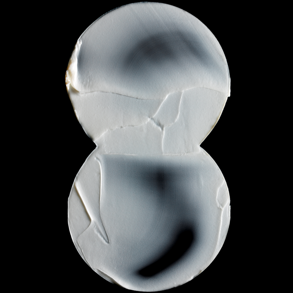 A clear, transparent glass or acrylic object with a double-humped, hourglass-like shape, photographed against a solid black background.