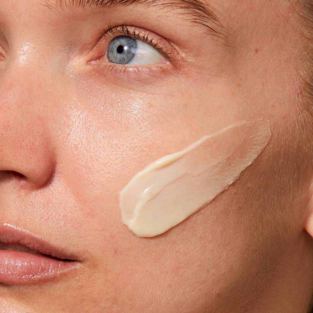 Close-up of a person's face with a light cream product applied to the cheek.