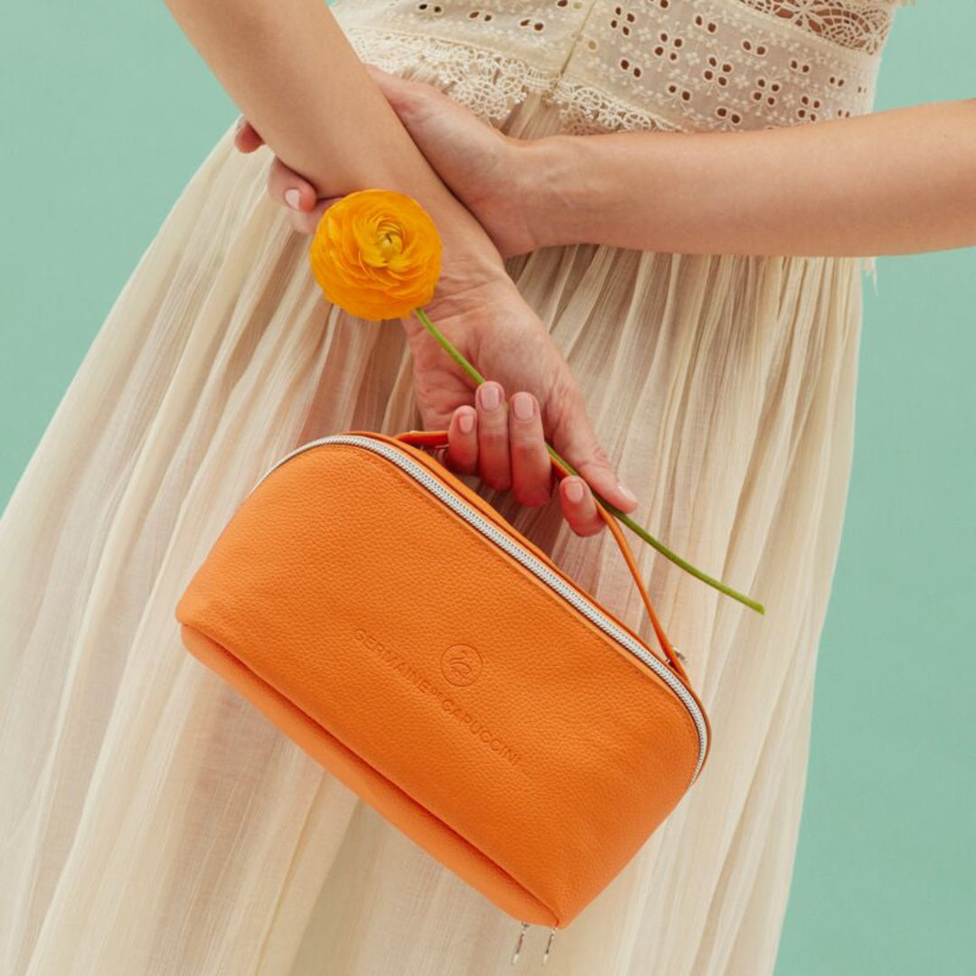 Person holding an orange clutch bag and a yellow flower against a teal background