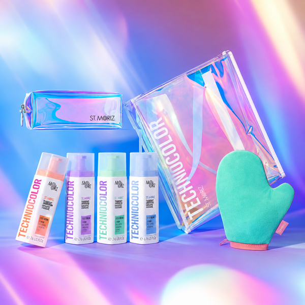 Technicolor hair dye set including four spray bottles in peach, purple, mint, and light blue, a holographic zip pouch, a large holographic storage bag, and a mint green oven mitt, arranged on a colorful iridescent studio background.