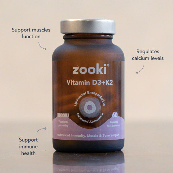 A brown supplement bottle labeled 'zooki Vitamin D3+K2' with a silver cap, shown on a light beige background with three callout text overlays describing benefits. The bottle is centered and the text points to muscle function, calcium levels, and immune health.