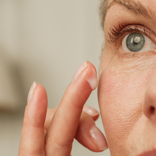 Close-up of a person's eye with a finger touching the skin around it.