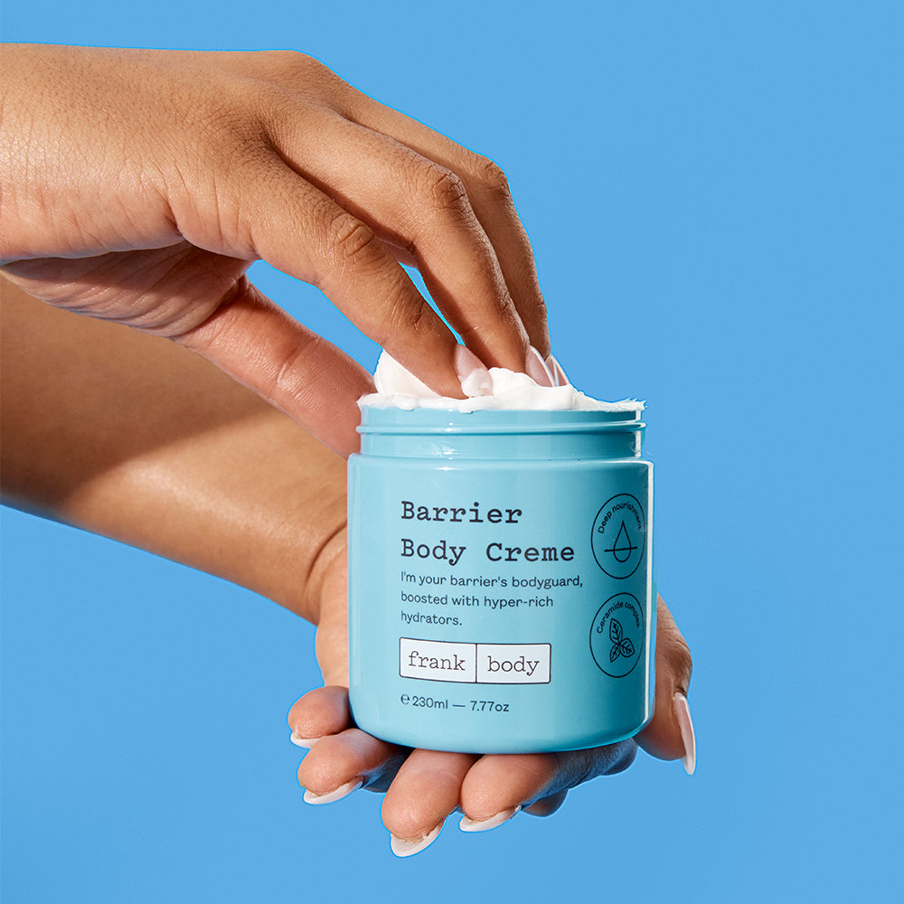 Hand holding a jar of Barrier Body Creme against a blue background