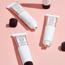 Three white lip balm tubes with black caps on a pink background