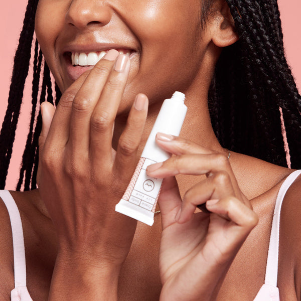 Woman holding a white tube of skincare product against a pink background