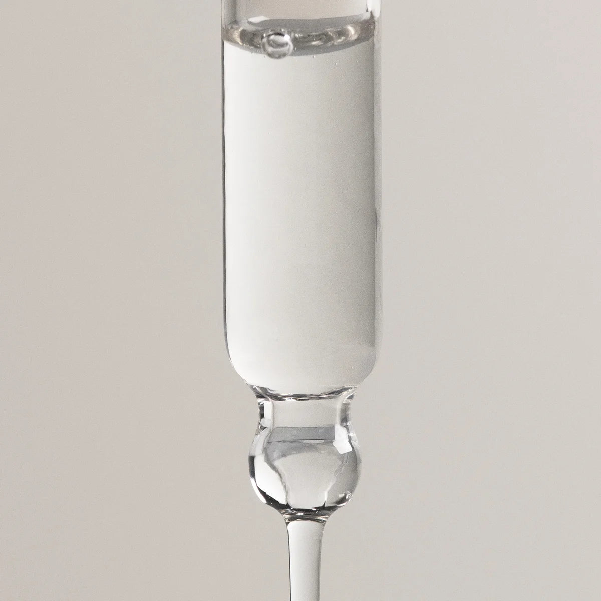A clear glass dropper pipette containing a white liquid, shown vertically against a neutral light gray background.