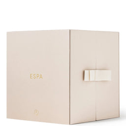 A square beige gift box with the brand name 'ESPA' printed in gold on the front, featuring a small gold emblem near the bottom and a white ribbon tied around the right side, set against a plain white background.