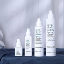 Collection of 'thisworks' deep sleep pillow spray bottles on a bed with a blurred background.