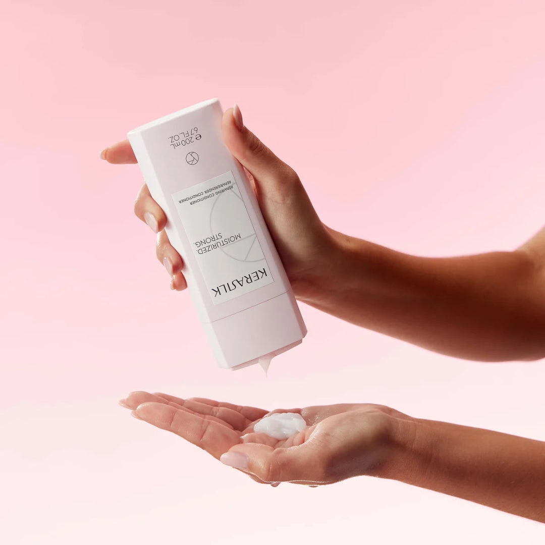 Person holding a white skincare product with a pink background