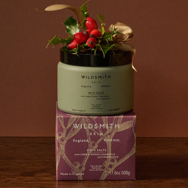 Wildsmith Skin bath salts with holly leaves and berries on a brown background
