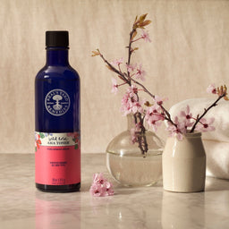Neal's Yard Remedies Wild Rose AHA Toner bottle next to a branch of small flowers