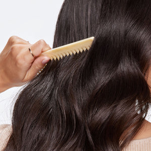 Person combing their wavy hair with a beige comb against a neutral background