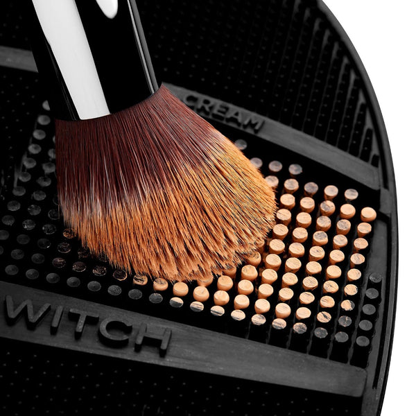 Makeup brush with brown bristles on a black surface with 'WITCH' branding.