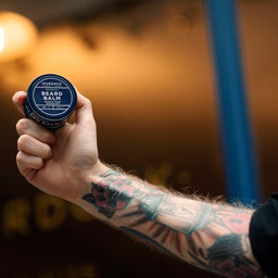 a tattooed arm holds the Murdock London Beard Balm 50ml tub into the air